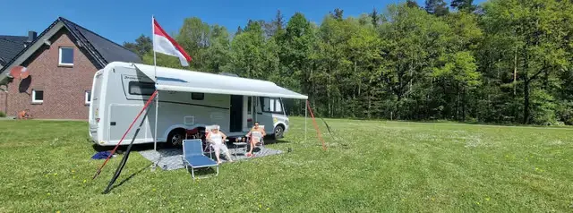 Wohnmobil mit Vorzelt und Fahne auf einer grünen Wiese, davor entspannen zwei Personen