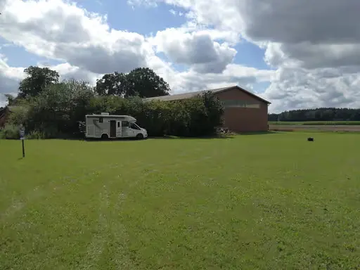 Wohnmobil auf grüner Wiese neben einem großen Scheunengebäude
