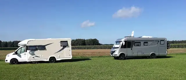 Zwei Wohnmobile stehen nebeneinander auf einer grünen Wiese am Rand eines Feldes